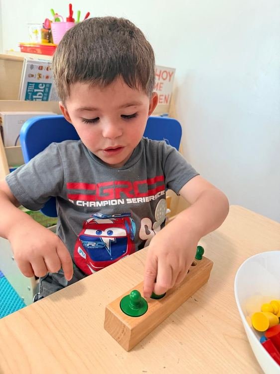A boy practicing fine motor skills with a wooden peg board