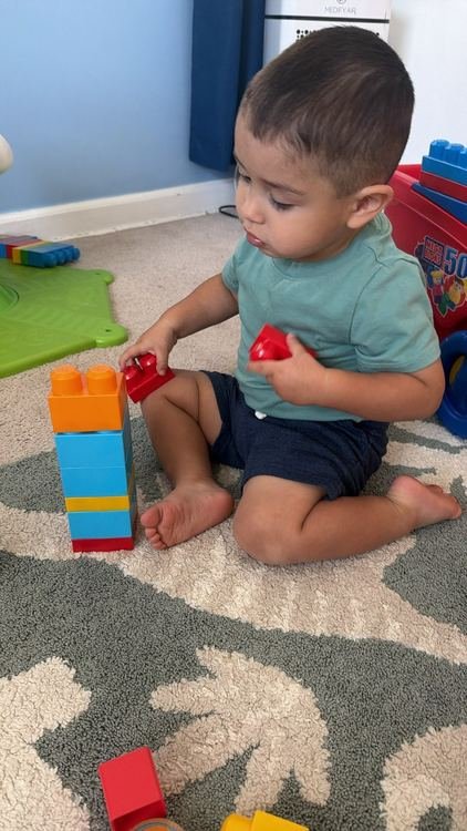 A toddler boy holding blocks beside his block tower