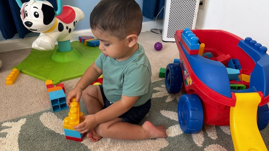 A toddler boy playing with blocks near a toy wagon