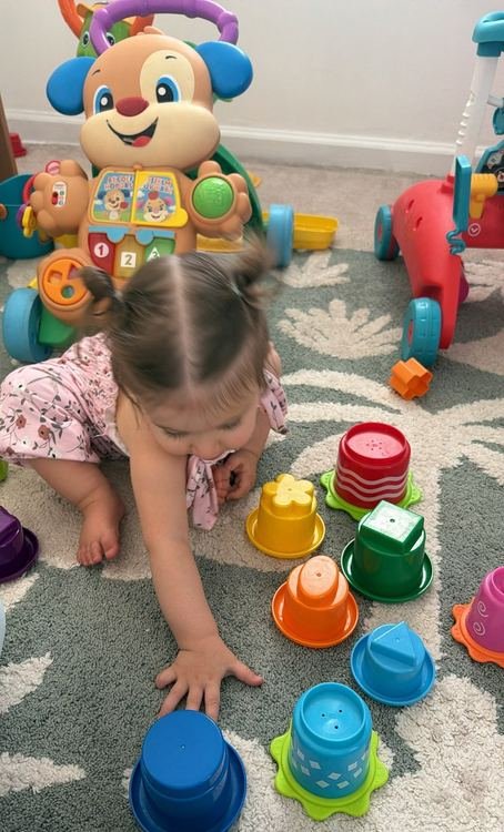A toddler girl reaching for colorful stacking cups