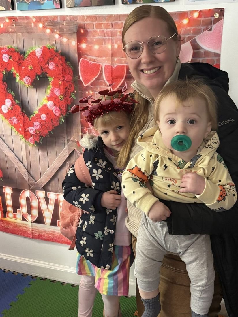 A teacher with two children at a Valentine's Day photo backdrop