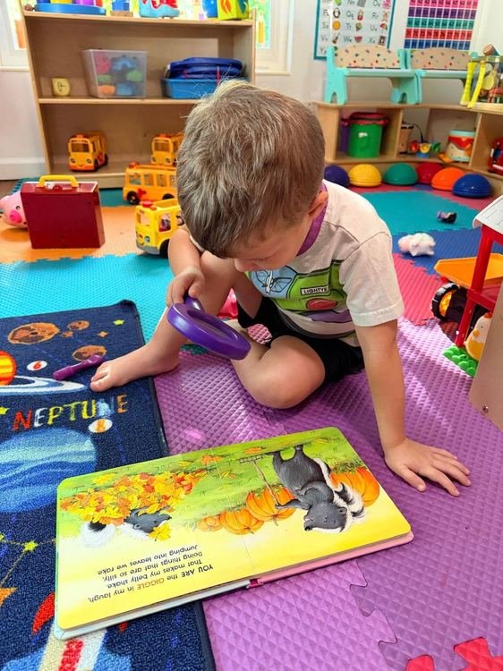 A boy reading a book with a magnifying glass