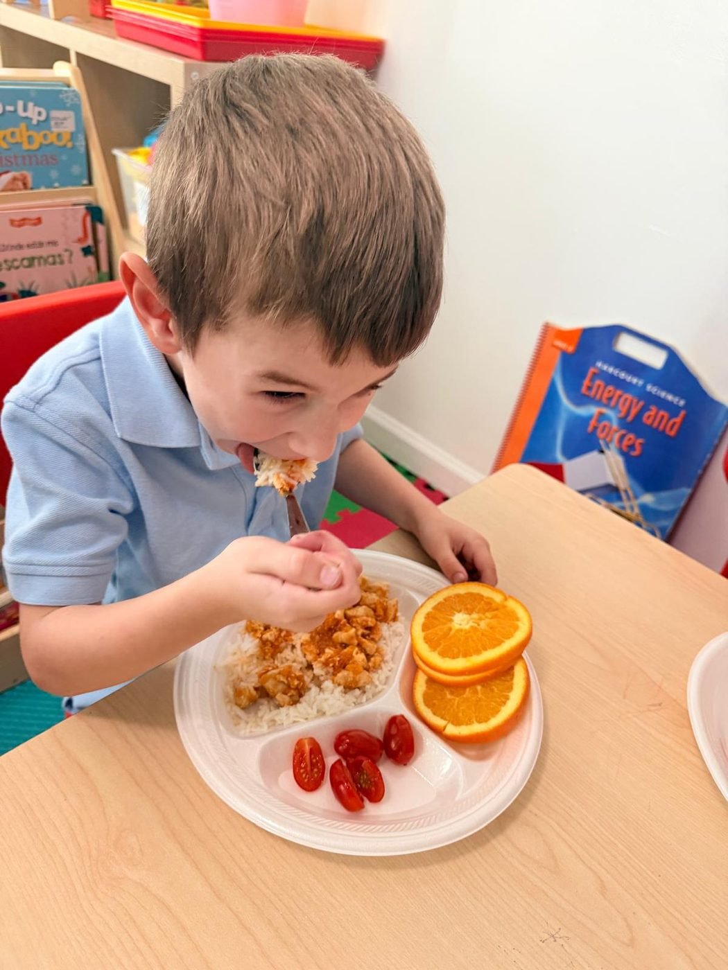 A boy enjoying a balanced meal of rice, chicken, cherry tomatoes, and orange slices at Aby Early Learning Center